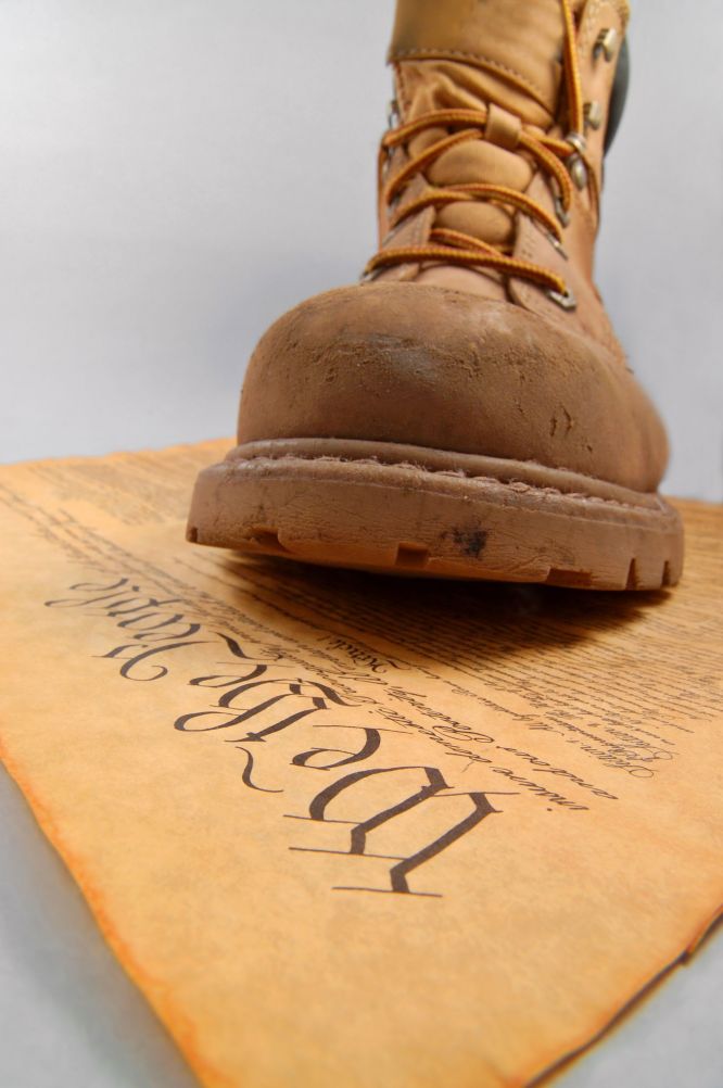 Close-up of a work boot resting on a faded parchment document with stylized text, symbolizing authority or conflict.