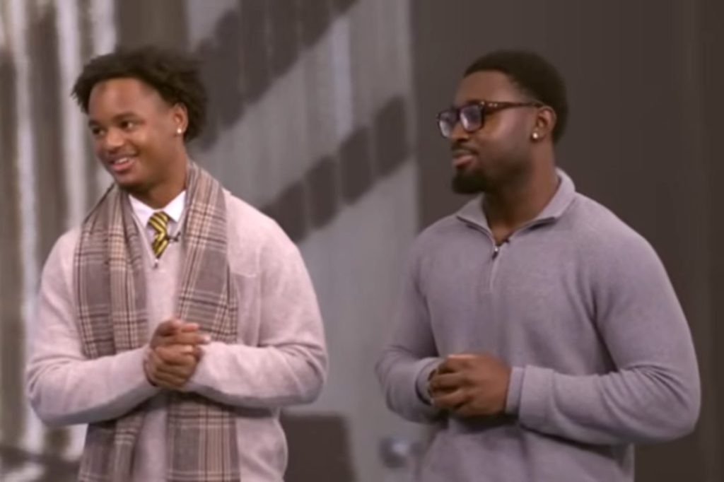 Two young men stand together, dressed in quarter-zip sweaters and a scarf, smiling and engaging in conversation.