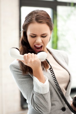 A frustrated woman in a business suit singing into a telephone receiver with an exaggerated expression.