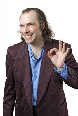 Man in a purple blazer and blue shirt smiling and making an 'OK' hand gesture.
