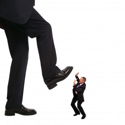 A large businessman in a suit is raising his foot above a smaller man in a suit, who appears to be in a defensive posture.