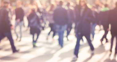 A blurred image of a crowded street, with people walking in various directions.