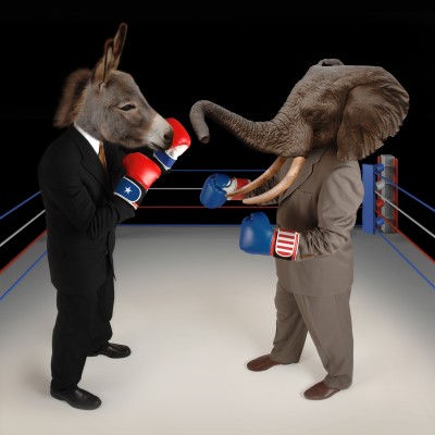 A donkey wearing a suit and boxing gloves facing an elephant in a suit and boxing gloves in a boxing ring.