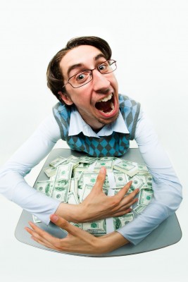A man with glasses and a blue argyle vest is enthusiastically surrounded by stacks of money on a table, expressing excitement.