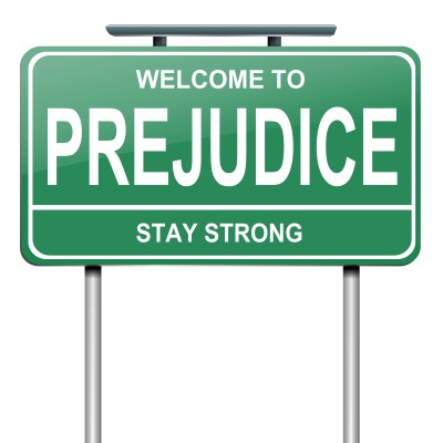 A green roadside sign that says 'WELCOME TO PREJUDICE' in large white letters, with the phrase 'STAY STRONG' below it.