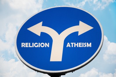 A road sign featuring two arrows pointing in opposite directions, labeled 'Religion' and 'Atheism', against a blue sky.